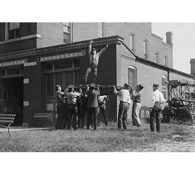 Buyenlarge Firefighter Jumps Into Net Held By Fellow Firemen - Photograph Print In Black;gray