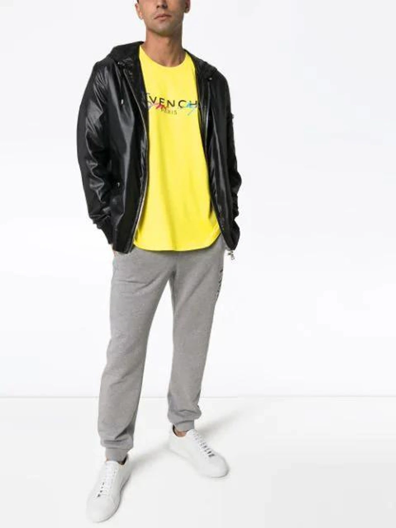 Farfetch's Post | Wearing: Givenchy Rainbow Logo Cotton T-shirt In Yellow; Balmain Faux Leather Hooded Jacket In Black; Versace Printed Logo Cotton Jersey Sweatpants In Grigio Chiaro