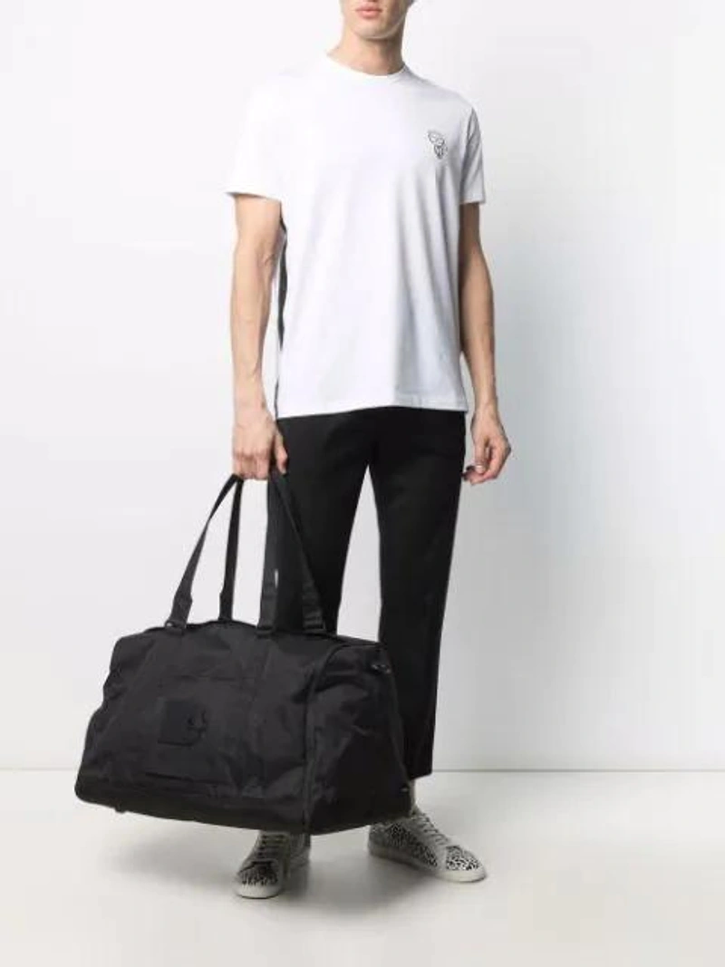 Farfetch's Post | Wearing: Karl Lagerfeld Appliqué Cotton-jersey T-shirt In White; Cmmn Swdn Tapered Drawstring Trousers In Black; Herschel Supply Co Large Zipped Holdall In Black