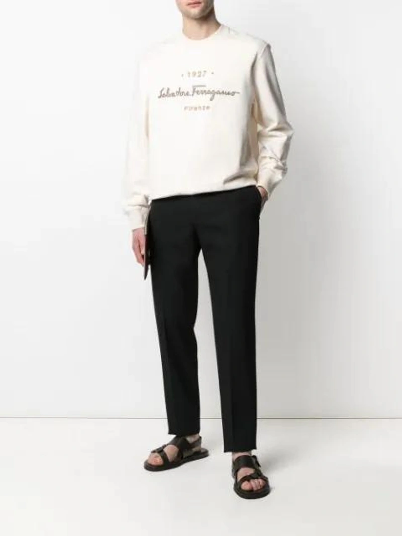Farfetch's Post | Wearing: Ferragamo Embroidered Logo Crew Neck Sweatshirt In Beige; Jil Sander Black Thynne Trousers; Loewe Logo Clutch Bag In Brown