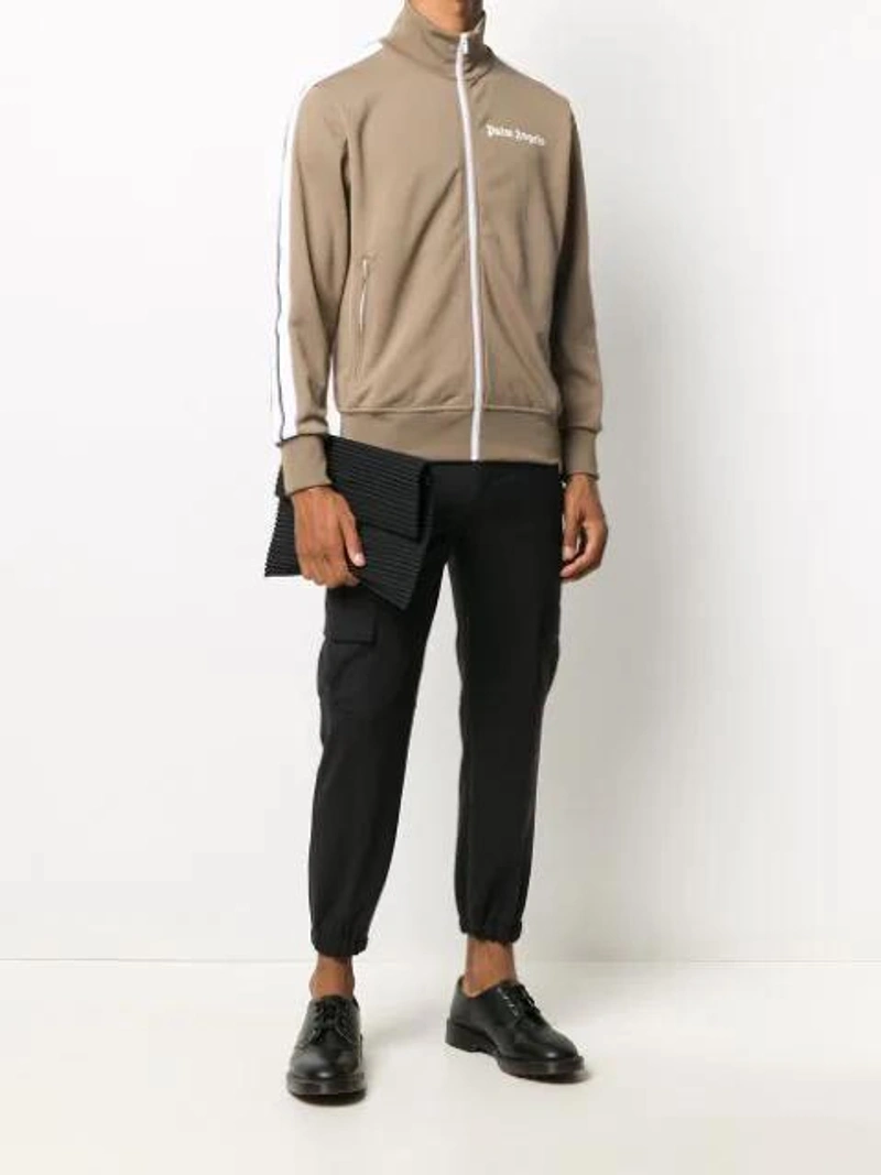 Farfetch's Post | Wearing: Palm Angels Side Panel Zip-up Sweatshirt In Brown; Neil Barrett Gathered-ankle Tailored Trousers In Black; Issey Miyake Homme Plisse Pleats Flat Bag In Black.