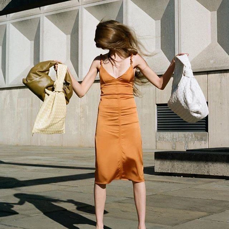 THELIST's Post | Wearing: Bottega Veneta Knotted Satin Dress In Black; Bottega Veneta Knotted-strap Satin Pencil Dress In Neutrals; Bottega Veneta Bv Twist Suede Clutch In Beige